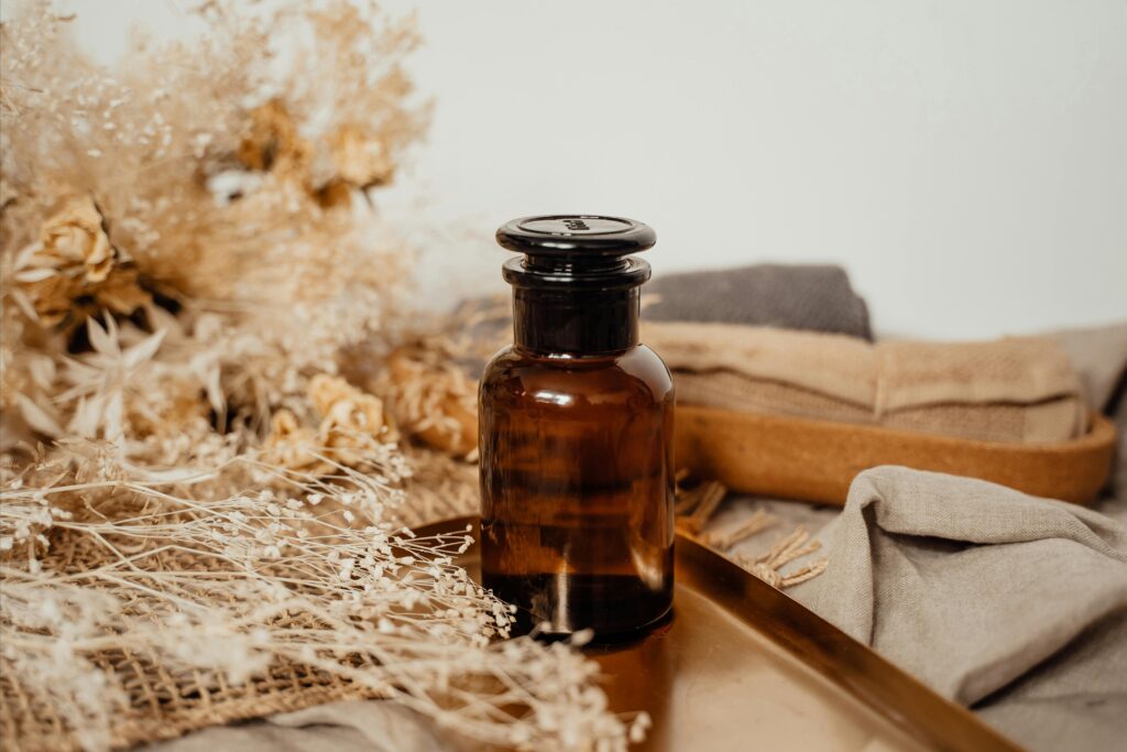 Amber glass bottle surrounded by dried flowers on a rustic surface, creating a vintage aesthetic.