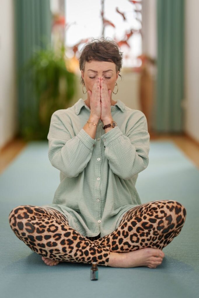 Svenja Beumers sitzt im Schneidersitz auf Yogamatte mit und inhaliert ein äthärisches Öl.